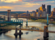 A sweeping, golden-hour illustration showing multiple iconic Pittsburgh bridges — Roberto Clemente, Smithfield Street, and Fort Pitt — spanning the rivers with the skyline rising in the distance.