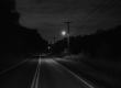 A vintage black-and-white photo of a quiet rural road in Western Pennsylvania at night, symbolizing the haunting legend of “Charlie No-Face” and his evening walks.