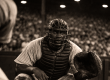 Baseball catcher in 1940s uniform crouches behind home plate at a packed Pittsburgh stadium, capturing the era when Josh Gibson was considered the greatest hitter in baseball.