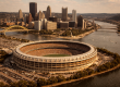 Aerial view of Three Rivers Stadium in Pittsburgh from across the Ohio River, the circular multipurpose stadium surrounded by the three rivers with the downtown skyline visible in the background.