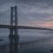Illustration of an eyebar suspension bridge over a river at winter dusk